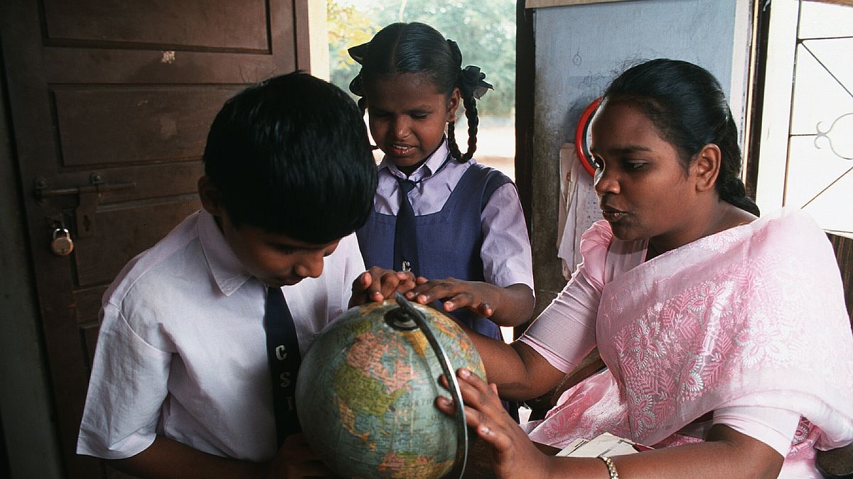 Low vision boy Karthik (11 years old) feeling the surface of a globe. A resource teacher is helping him. In the middle between them there is a classmate of Karthik. She is also touching the globe. The picture was taken in the resource room  of a school integrating handicapped children in Coimbatore, India.