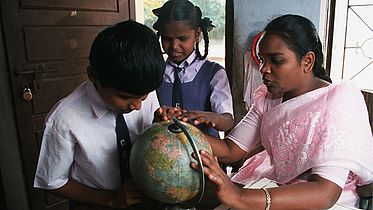 Low vision boy Karthik (11 years old) feeling the surface of a globe. A resource teacher is helping him. In the middle between them there is a classmate of Karthik. She is also touching the globe. The picture was taken in the resource room  of a school integrating handicapped children in Coimbatore, India.