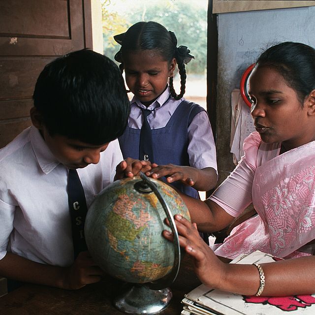 Low vision boy Karthik (11 years old) feeling the surface of a globe. A resource teacher is helping him. In the middle between them there is a classmate of Karthik. She is also touching the globe. The picture was taken in the resource room of a school integrating handicapped children in Coimbatore, India.