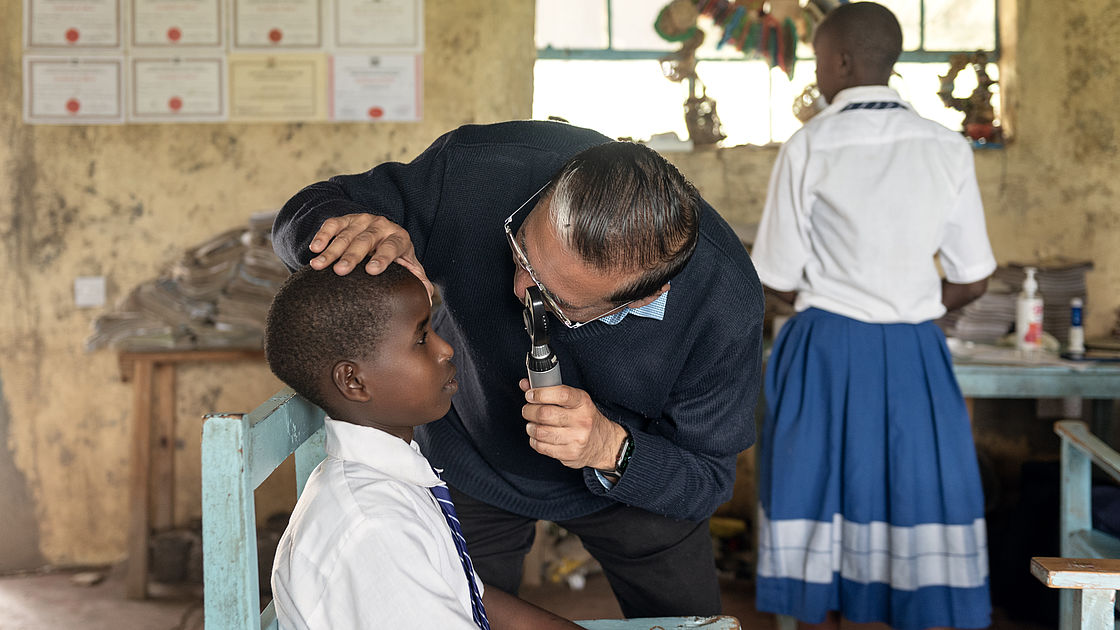 A man is examining the eyes of a student. 