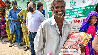 A man carrying a bag of food is smiling. Other people stand behind him